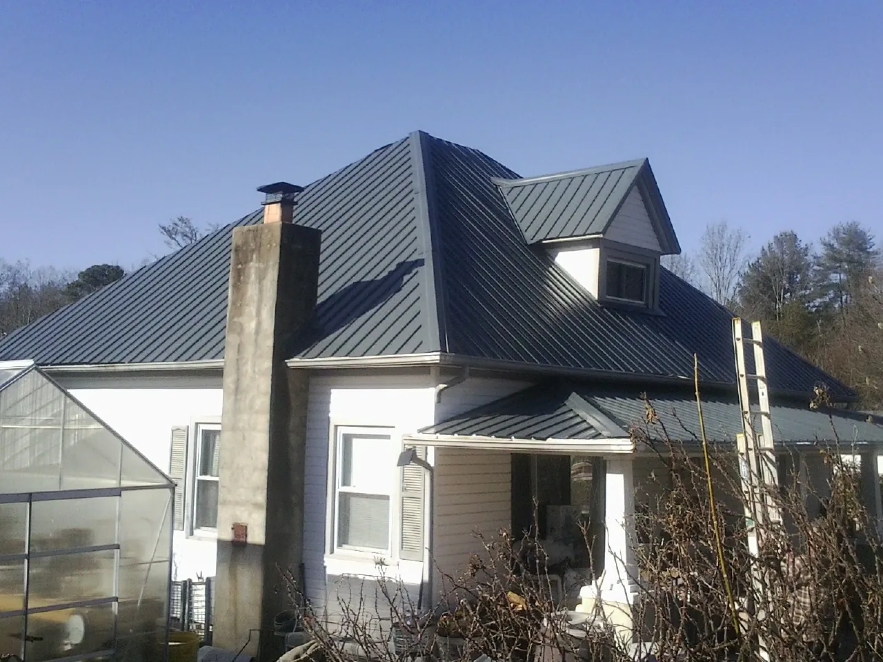 Dark blue standing seam metal roof on a white farmhouse with dormer — Slate & Tile Roof Repair by Roofing Brothers in Rock Cave