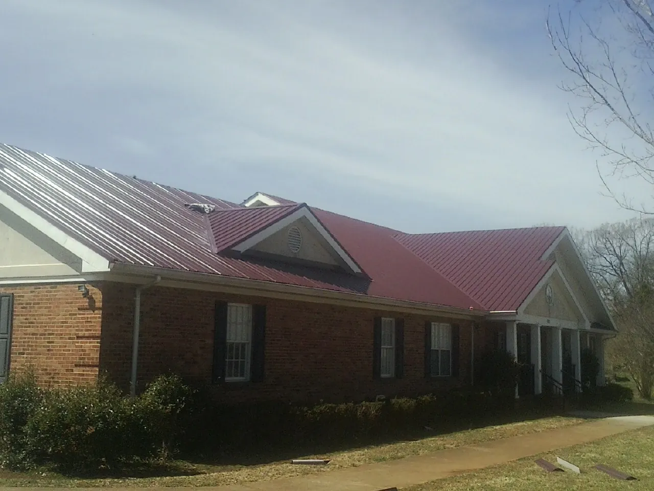 Red metal roof with gabled entries on a long brick building, from a Hail Damage Roof Repair job in Rock Cave