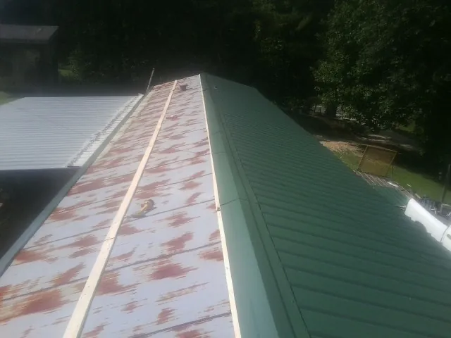 Old rusted panels beside newly installed green metal roofing — Wind Damage Roof Repair by Roofing Brothers in Rock Cave