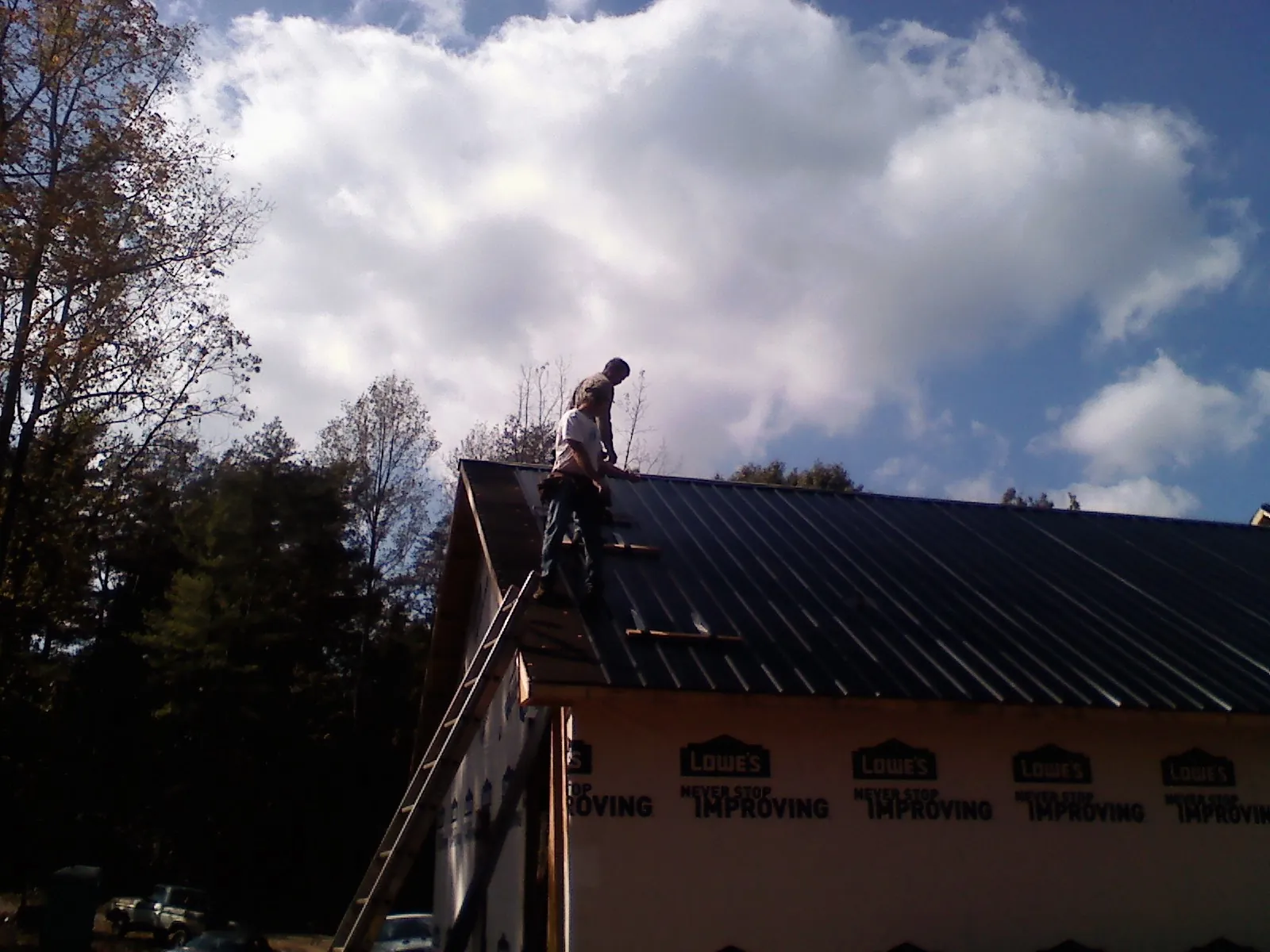 Roofer fastening dark metal panels high against a cloudy sky, from a Roof Inspection job in Rock Cave