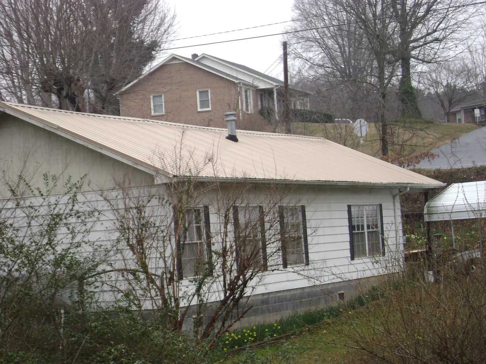 Tan metal roof on a white sided house set into a hillside — Commercial Roofing by Roofing Brothers in Rock Cave